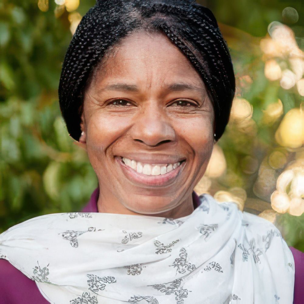 maire is a woman of color in box braids, with a white scarf draped over her shoulders against a purple garment